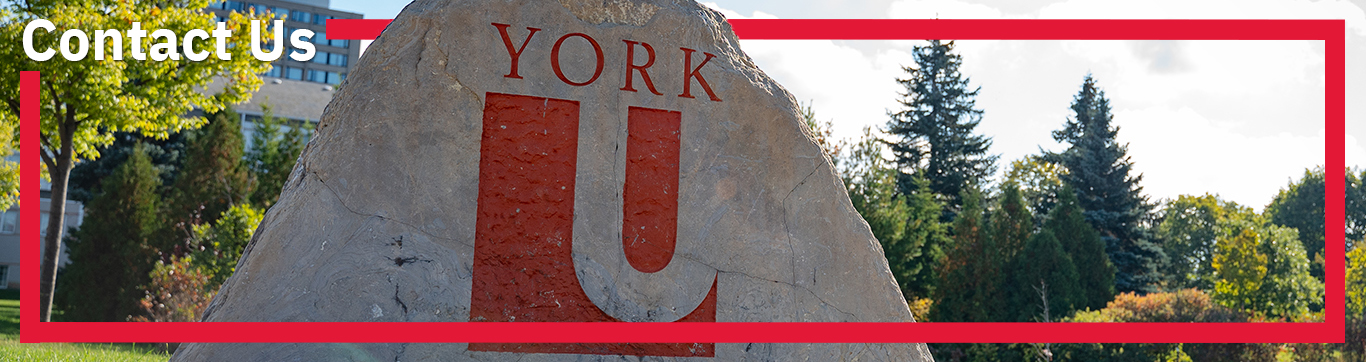 There is a large beige rock with the York University logo painted onto the surface. There are trees in the background and a red border outlines the image. The words 'Contact Us' are printed in white in the top left hand corner.